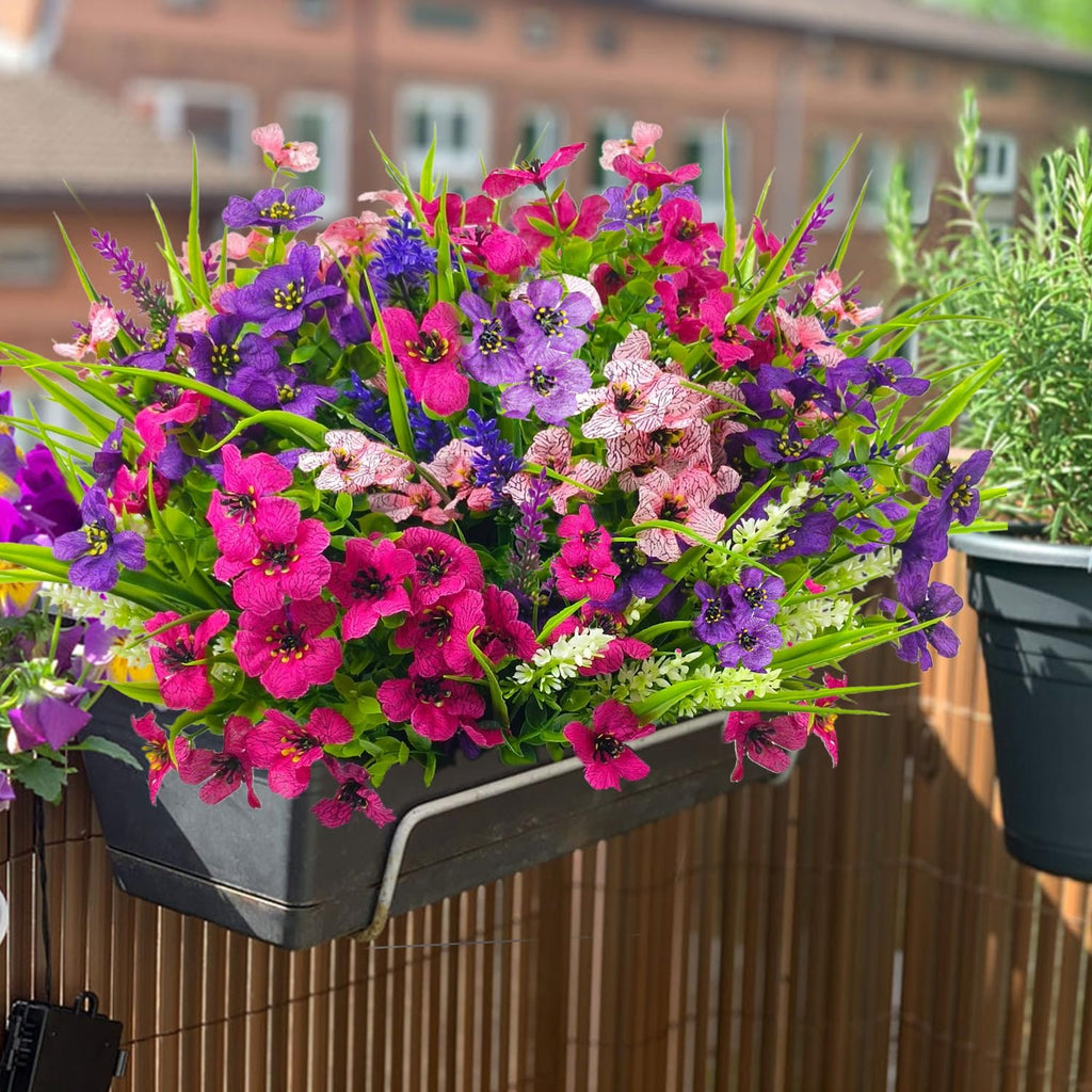 Mixed color artificial flowers in a black planter box on a balcony railing