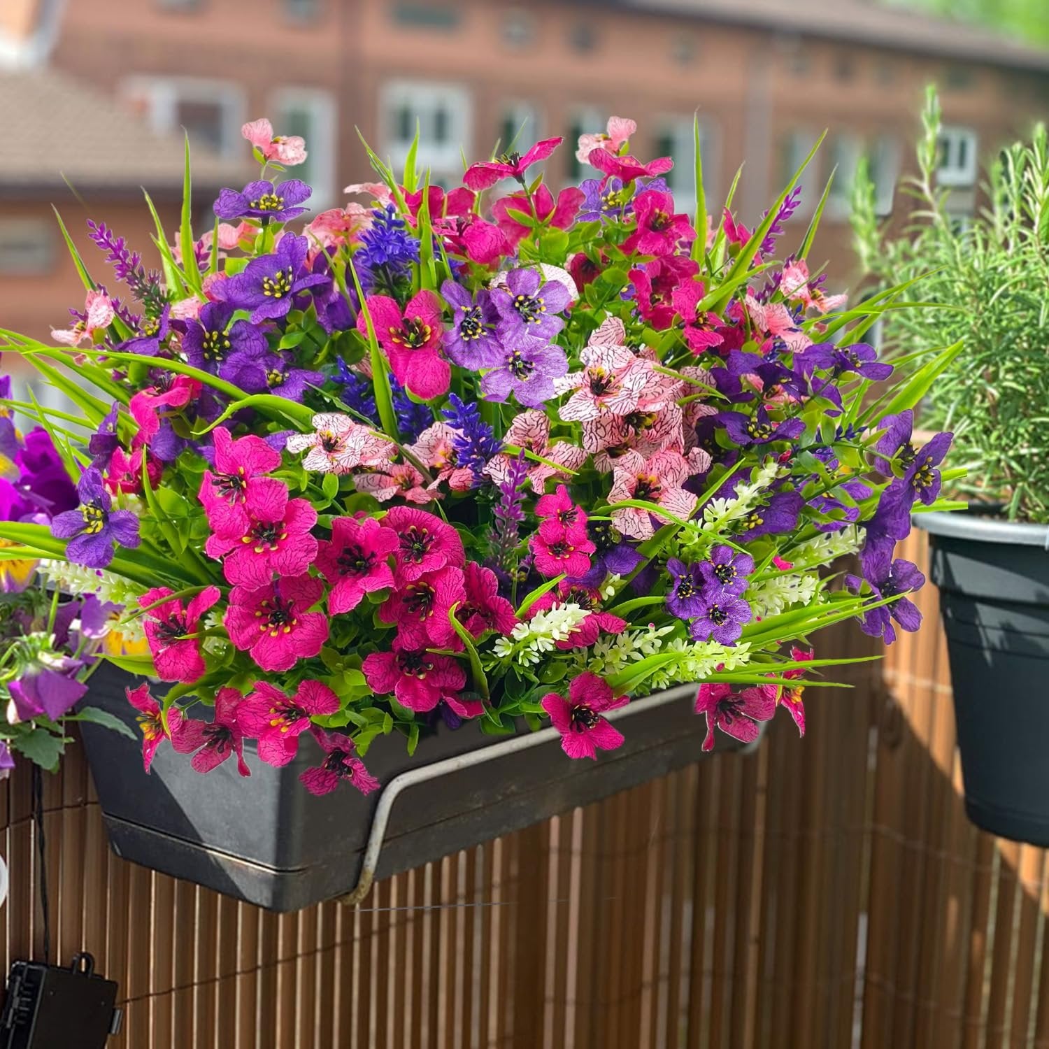 Mixed color artificial flowers in a black planter box on a balcony railing
