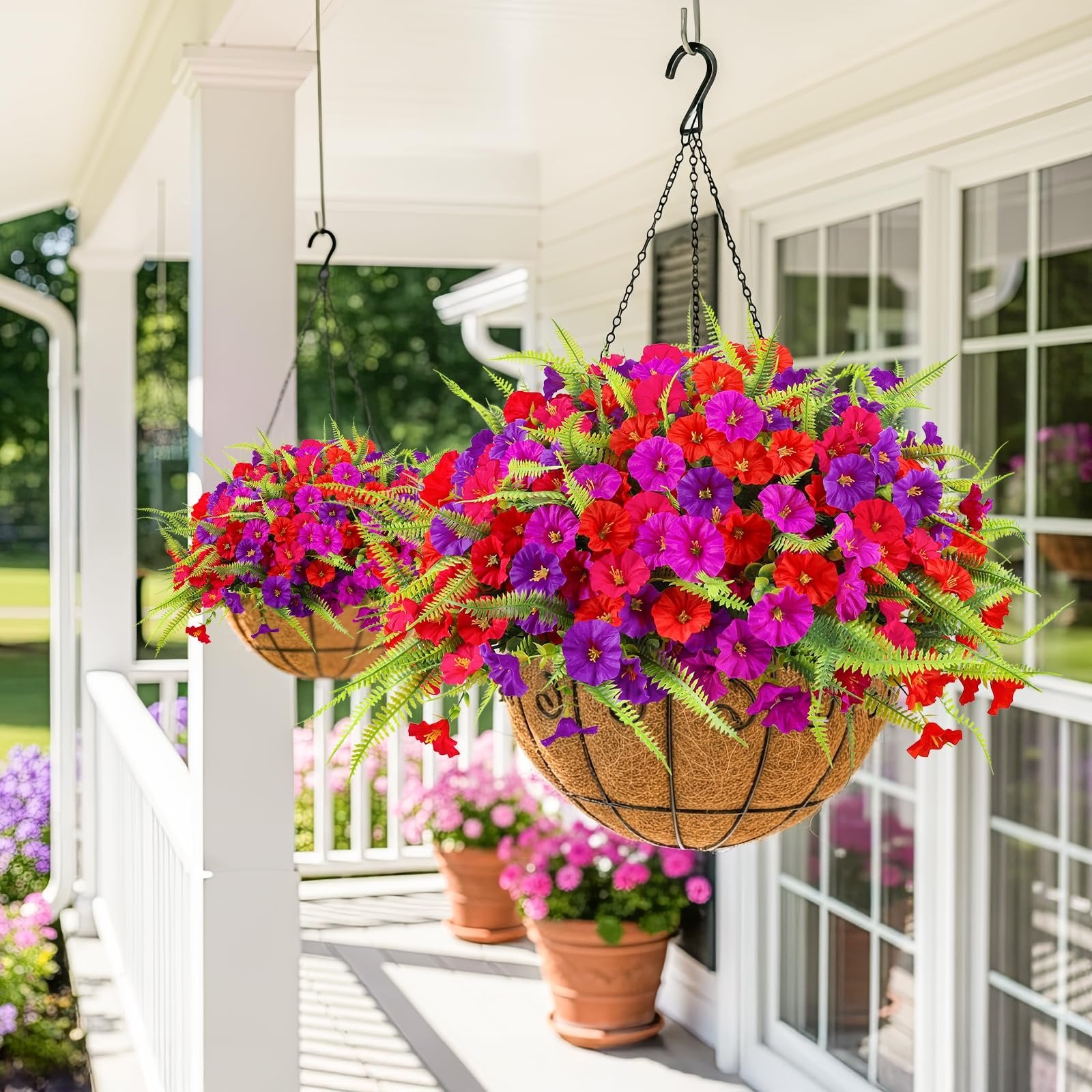 Two hanging baskets filled with artificial red and purple petunias and ferns on a porch.