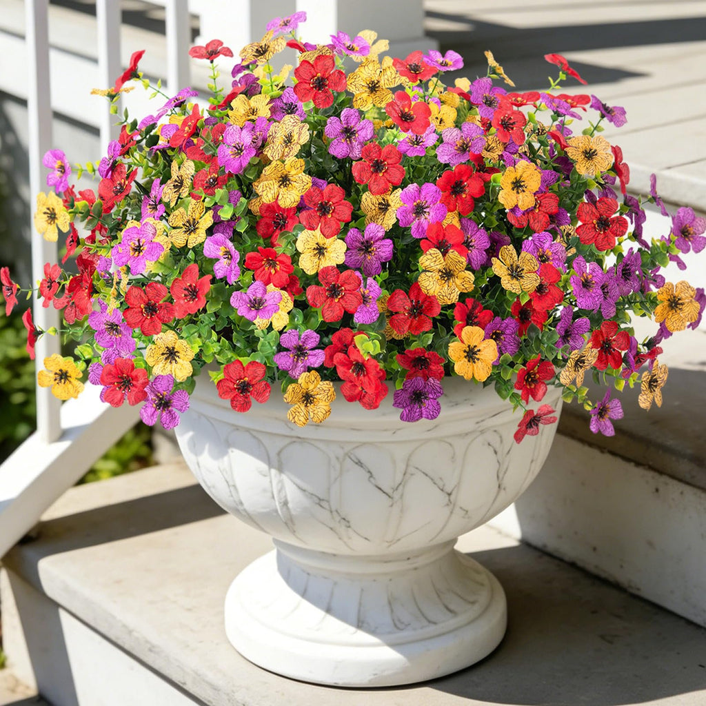 Artificial daisy flowers in red, purple, and yellow in a white marble-patterned planter on a porch.