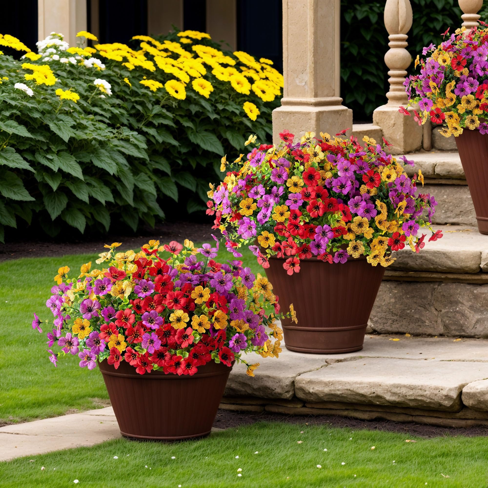 Two brown planters filled with colorful artificial daisy flowers and eucalyptus leaves on a stone patio and lawn.