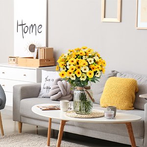 Bouquet of 12 mixed color artificial daisy silk flowers in a glass vase on a coffee table in a living room setting.