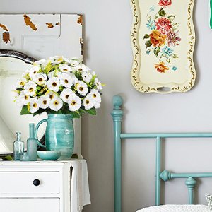 Bouquet of 12 artificial white daisy silk flowers in a teal pitcher on a white dresser.