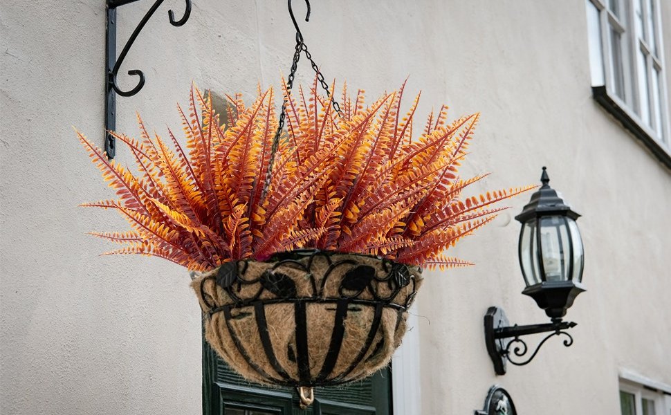 Hanging basket filled with artificial orange and red fall fern foliage, attached to a building exterior.