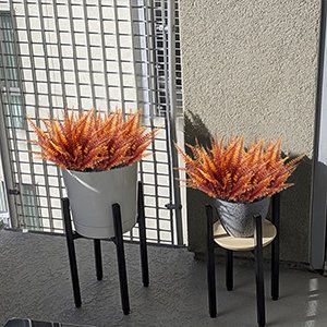 Two potted artificial fall fern and mum plants on stands on a balcony.