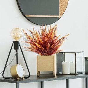 Artificial fall fern and mum plant in a wooden planter on a shelf with a lamp and clock.