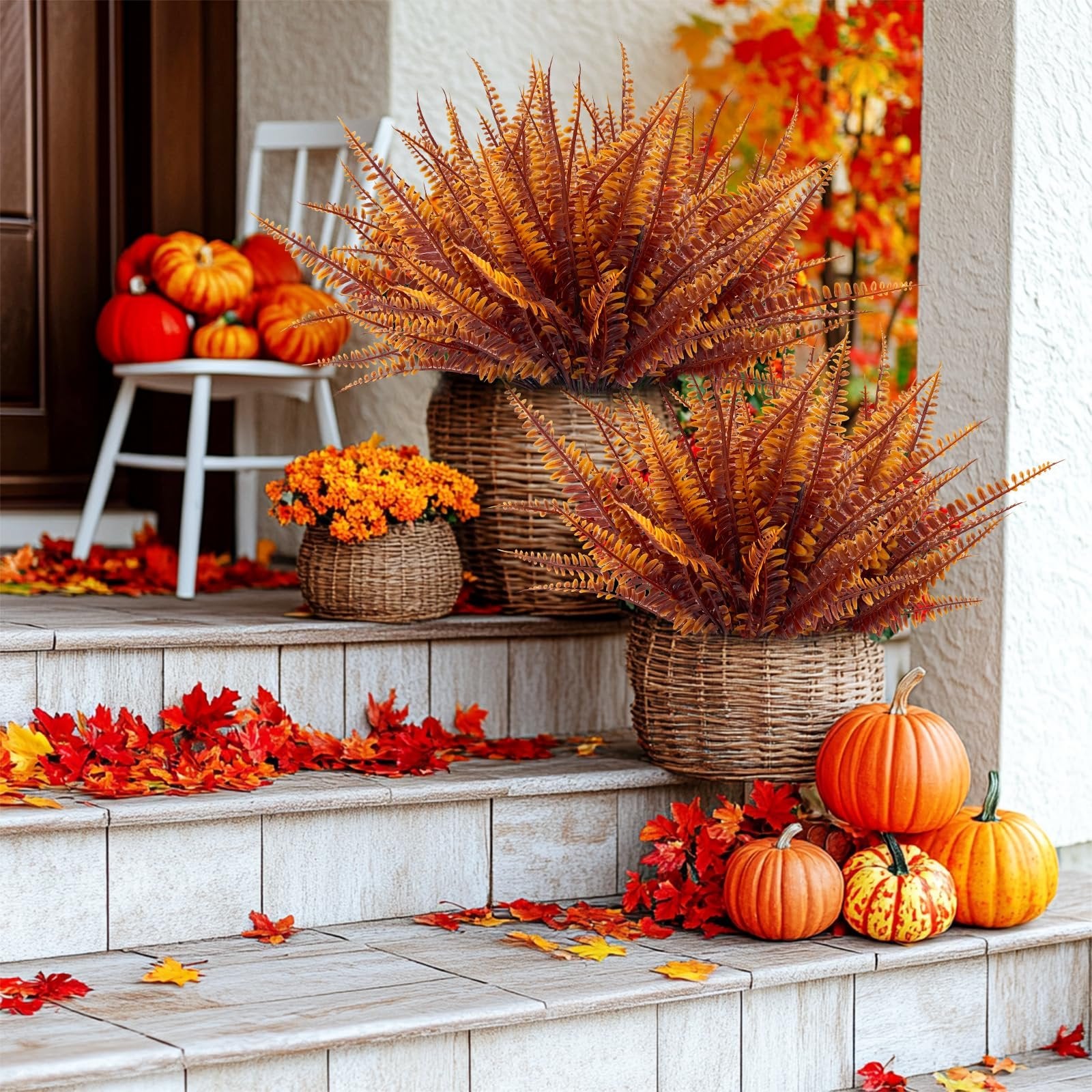 Autumn porch decor with artificial ferns in baskets, pumpkins, and scattered fall leaves on steps.