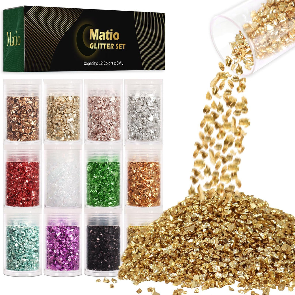 Twelve small jars of crushed glass glitter in various colors, with a pile of gold glitter spilling from a jar.