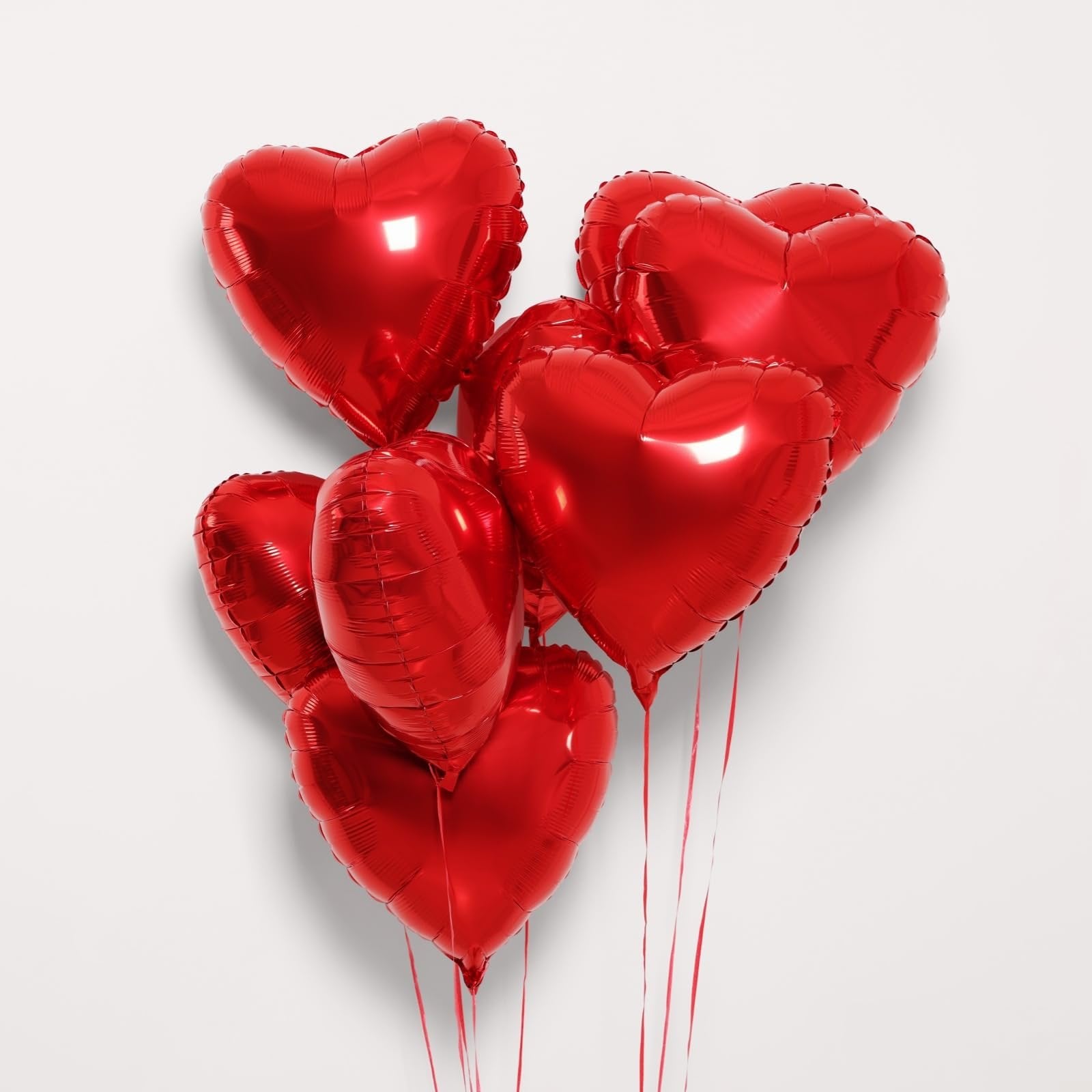 Group of red heart-shaped foil balloons with red ribbons against a white background