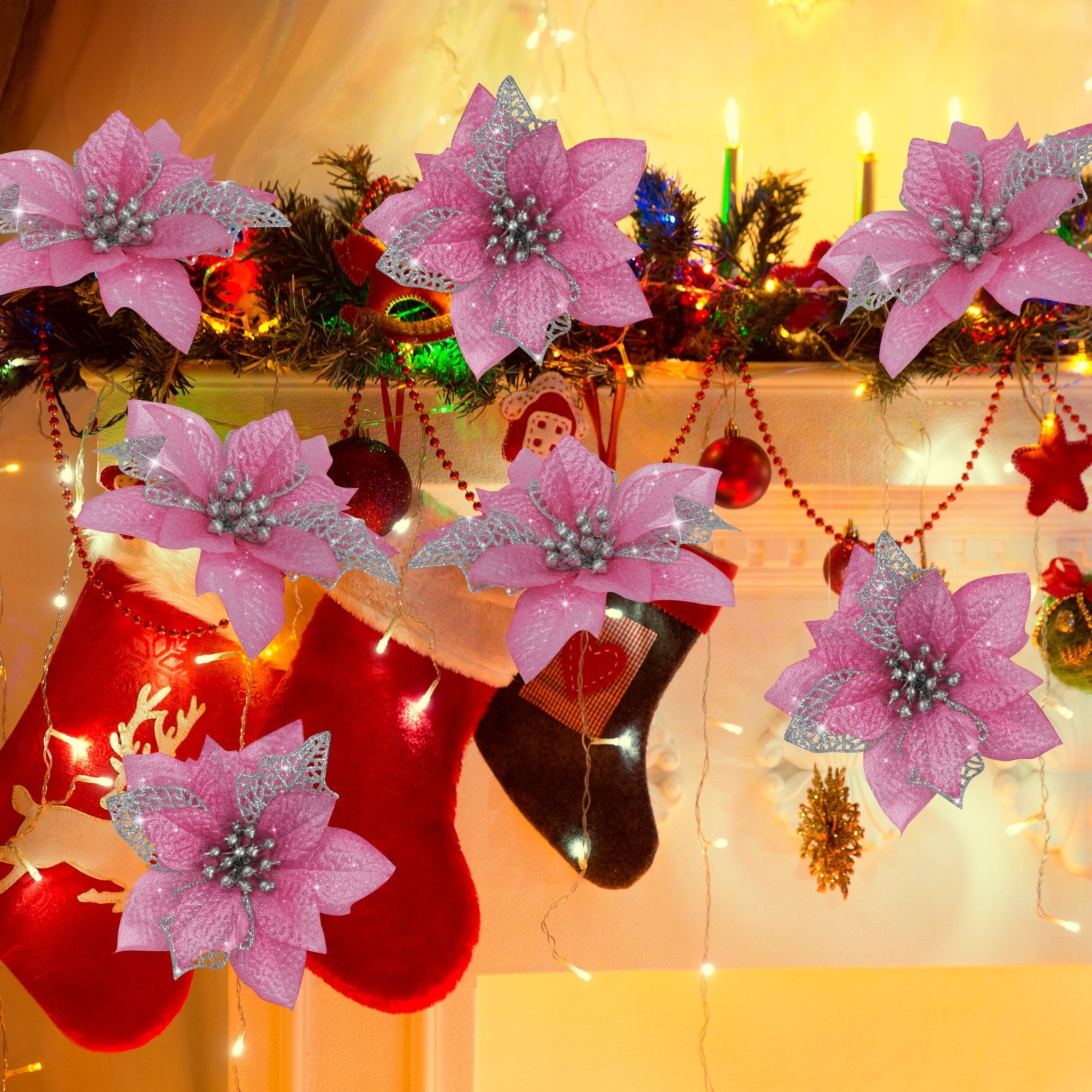 Six pink glitter poinsettia flowers with silver accents are arranged around Christmas stockings and garland on a mantelpiece.