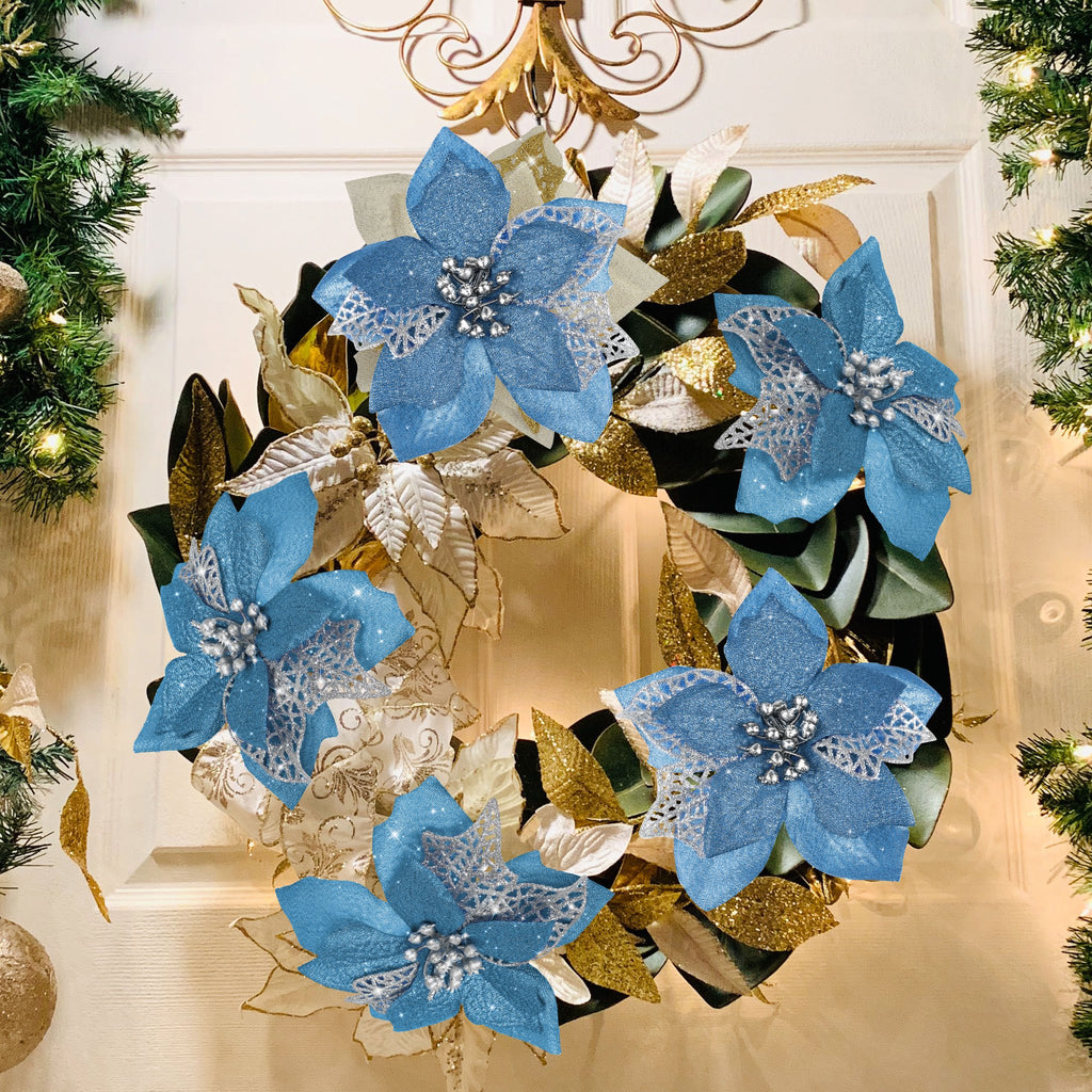 Christmas wreath with blue poinsettia flowers and gold accents on a white door with greenery and lights