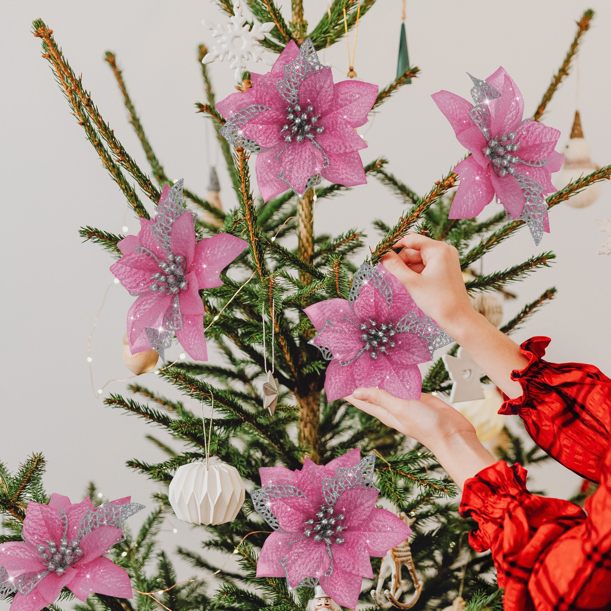 Hands decorating a Christmas tree with pink glitter poinsettia ornaments