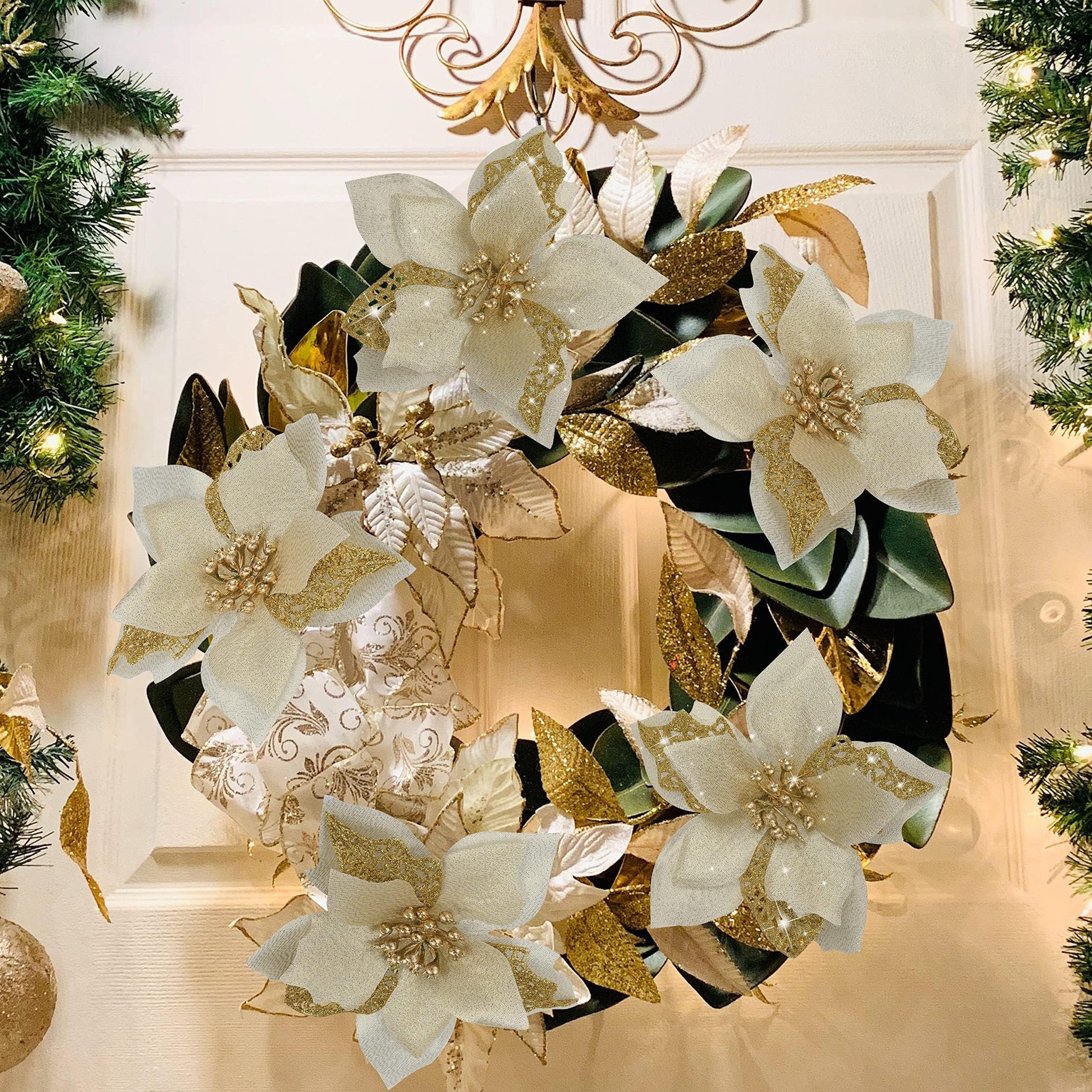 Christmas wreath with white and gold poinsettia flowers and glitter leaves, hanging on a white door with garland lights.