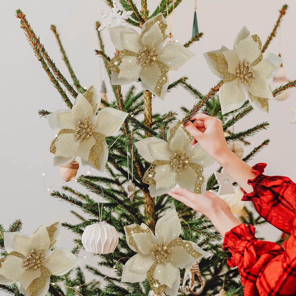 Hands decorating a Christmas tree with gold glitter poinsettia ornaments and fairy lights.