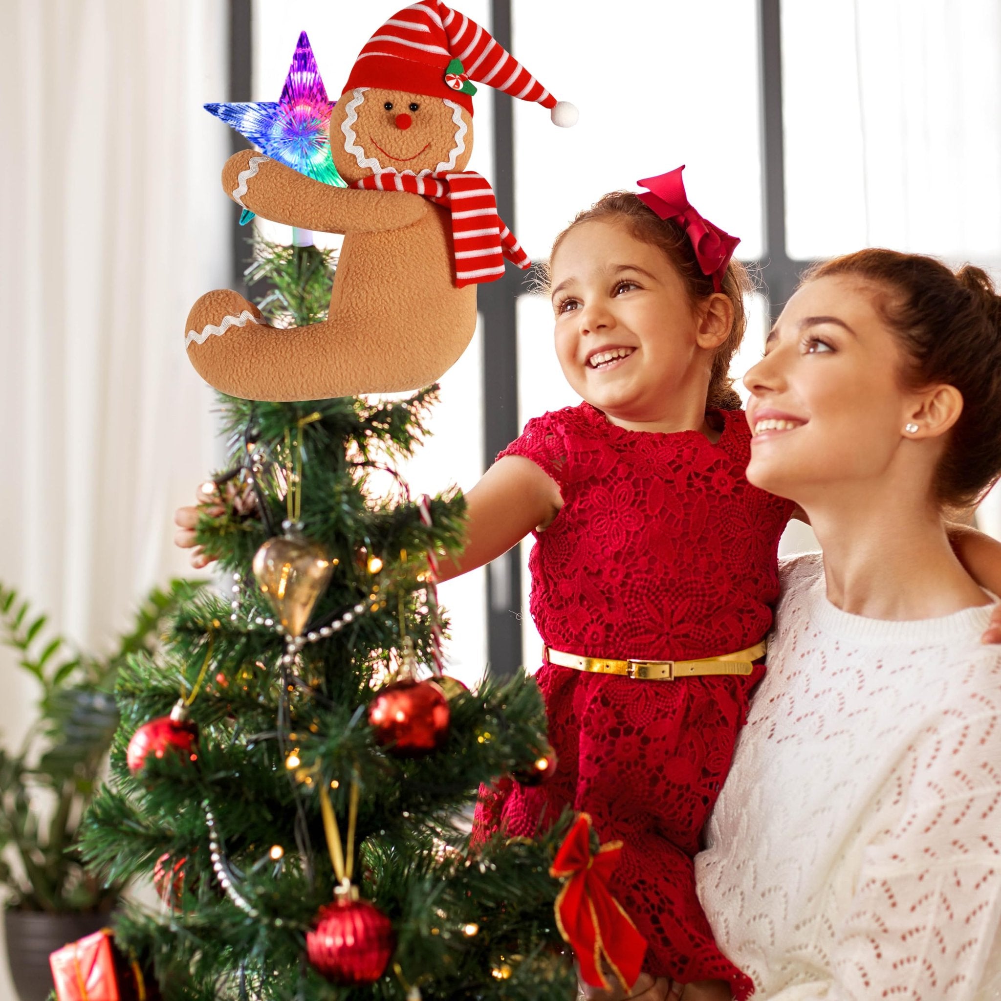 Gingerbread man tree topper with lighted star on Christmas tree with mother and daughter