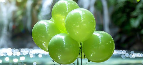 Bunch of bright green pearlized latex balloons floating in front of a blurred waterfall and bokeh lights