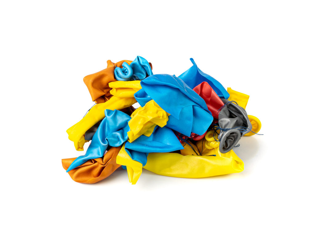 Pile of deflated latex balloons in assorted colors including orange, yellow, blue, red, and gray, on a white background.