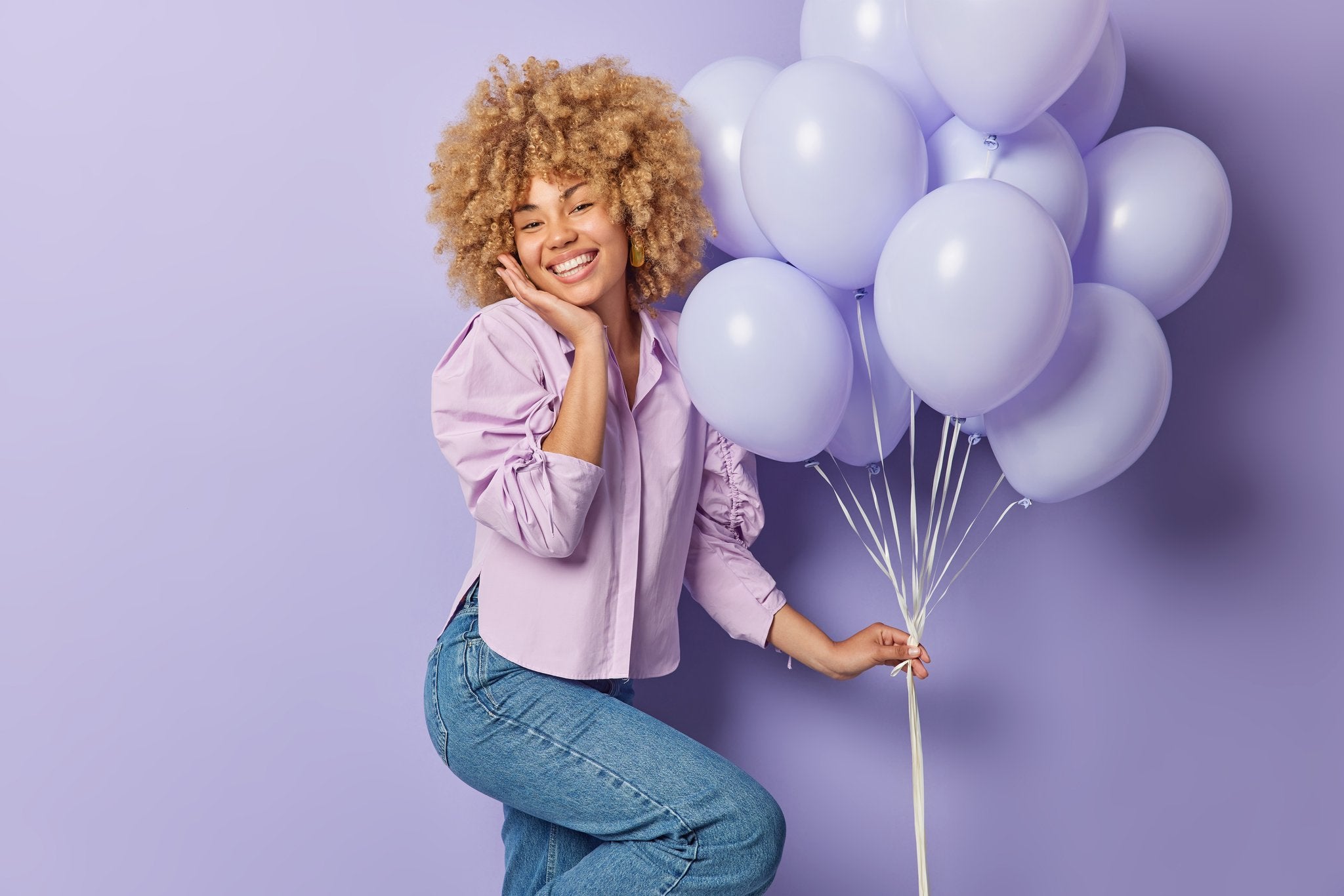 Woman holding a bunch of light purple balloons against a purple background