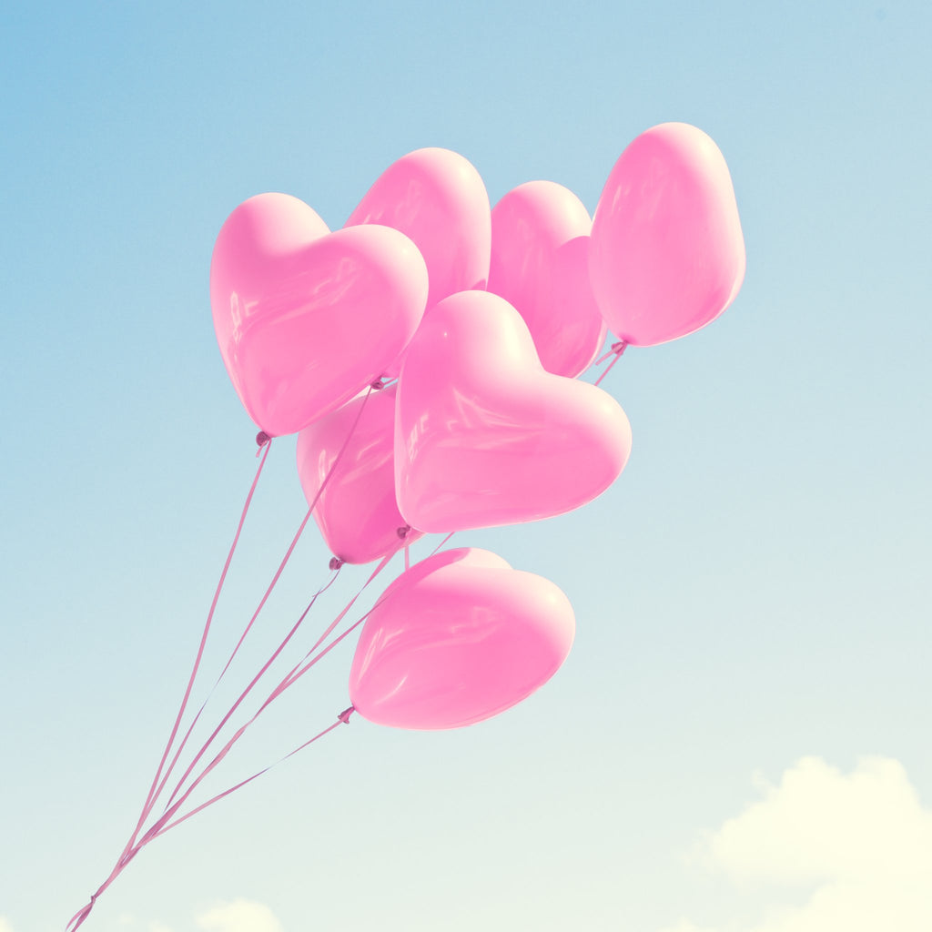 Pink heart-shaped balloons floating against a pale blue sky with wispy clouds.