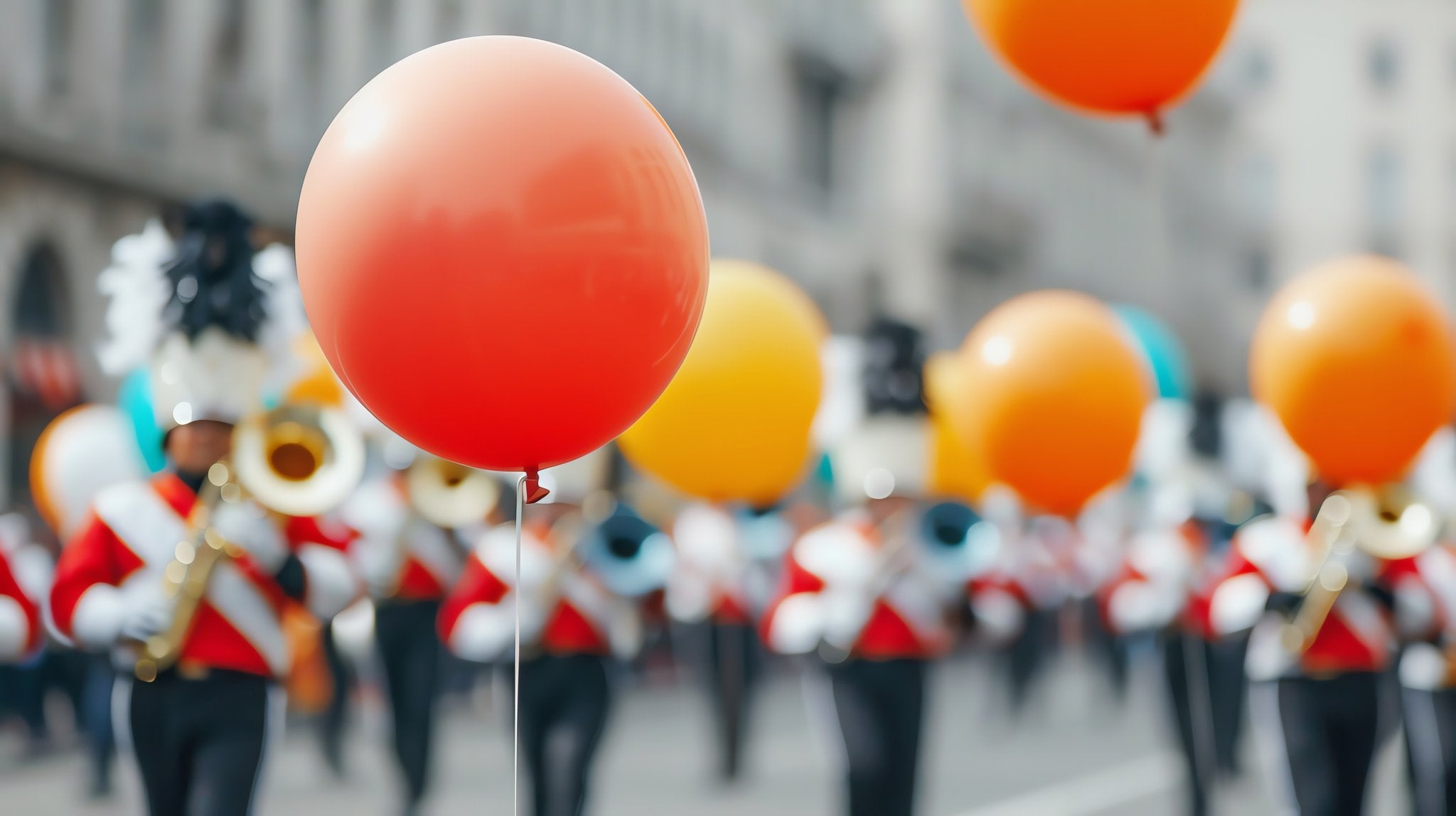 Close-up of a red balloon floating above a marching band in a parade, with other balloons visible in the background.