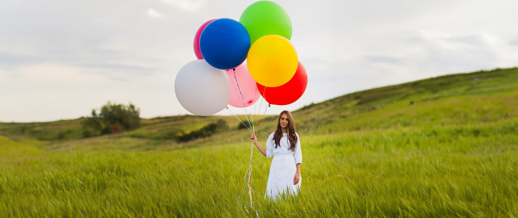 Woman holding a bunch of colorful balloons in a grassy field