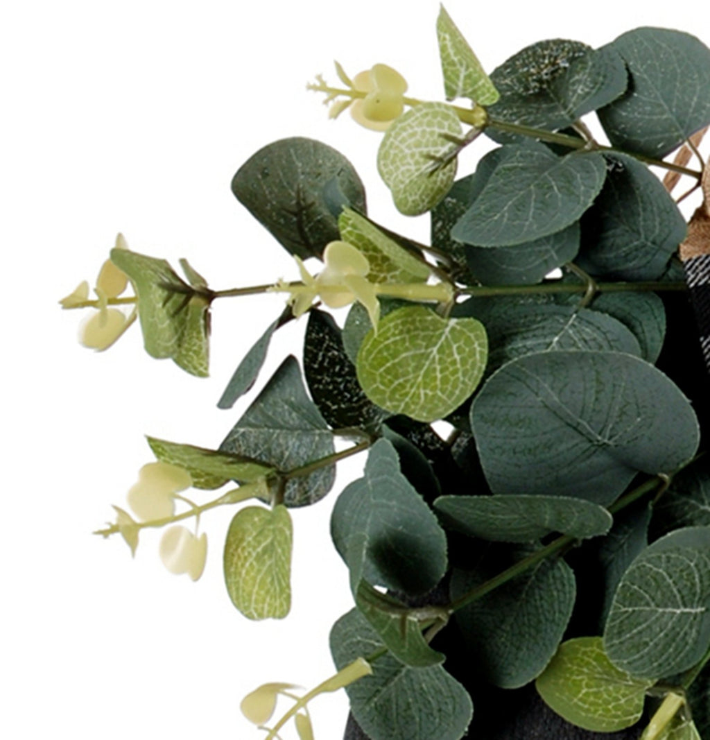 Close-up of a eucalyptus wreath with a plaid bow on a white background.