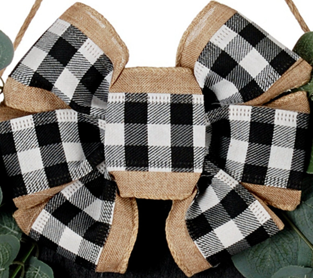 Close-up of a black and white buffalo plaid bow with burlap trim and faux eucalyptus leaves.