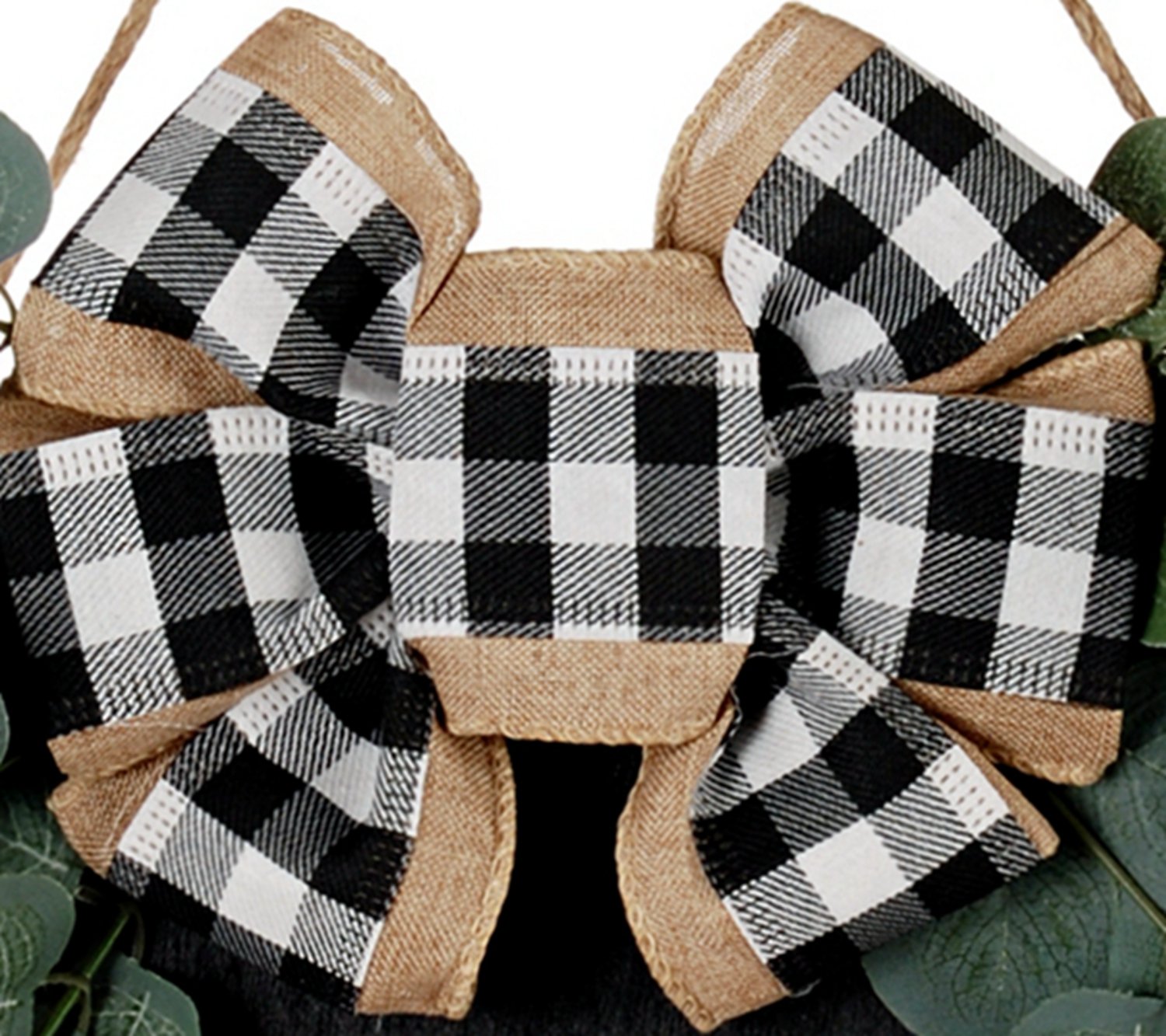 Close-up of a black and white buffalo plaid bow with burlap trim and faux eucalyptus leaves.