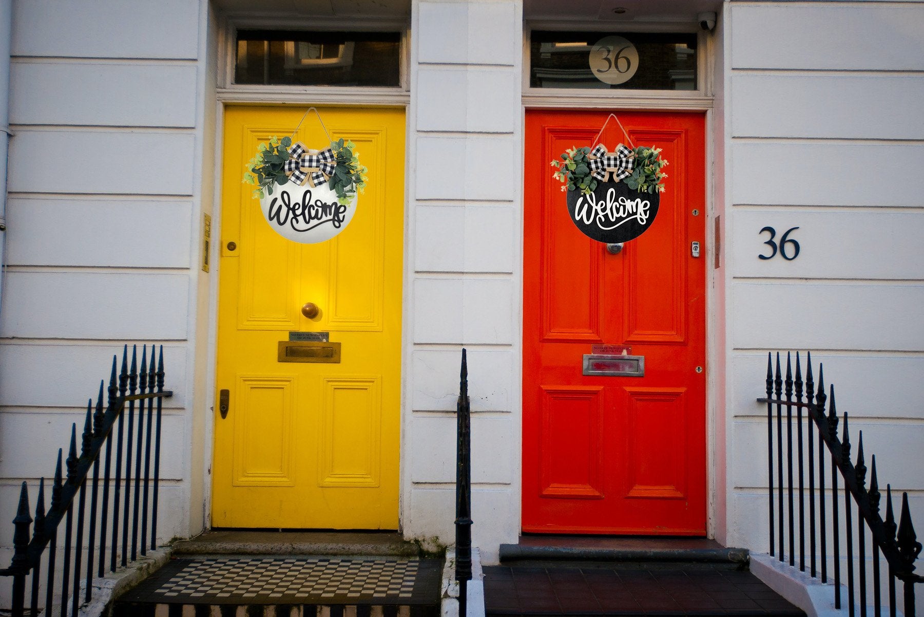 Two round wooden welcome signs with eucalyptus wreaths and plaid bows hanging on colorful doors.