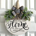 Round wooden welcome sign with greenery and black and white striped bow, reads 'Bless This Home And All Who Enter'