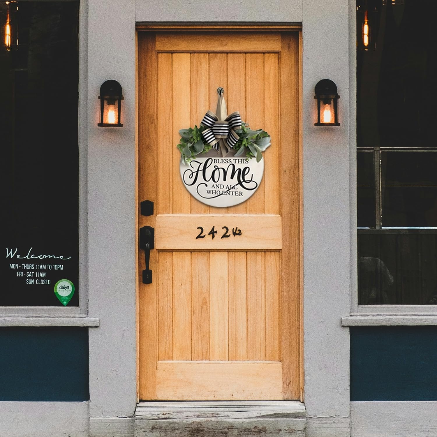 Round wooden welcome sign with greenery and bow hanging on a wooden door, displaying house number 24242.