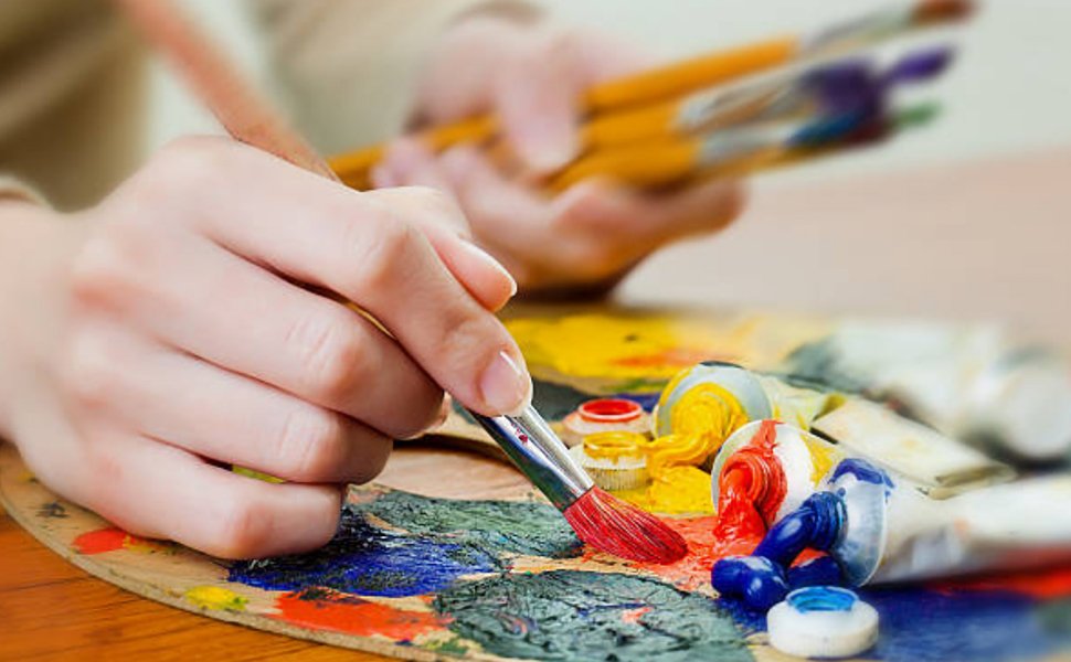 Artist's hands mixing neon oil paints on a wooden palette with brushes