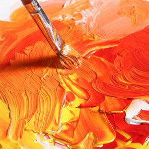 Paintbrush mixing vibrant neon orange and yellow oil paints on a palette