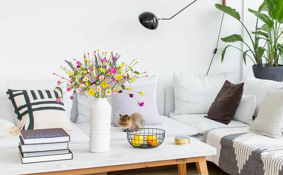 Artificial spring floral arrangement with daisies, wildflowers, and berries in a white vase on a coffee table.
