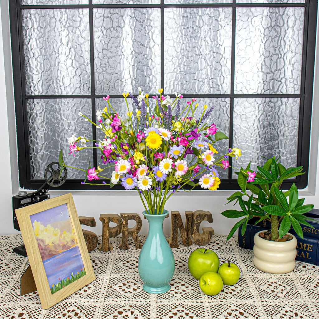 Vase of colorful artificial spring flowers with daisies and wildflowers, set on a lace tablecloth with decorative wooden letters spelling SPRING.