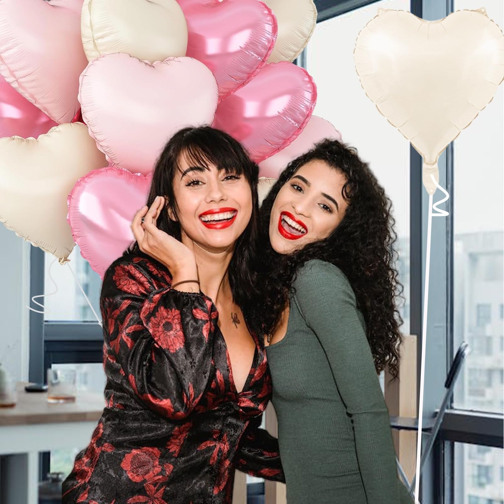 Two smiling women holding a cluster of heart-shaped foil balloons in pink and cream colors.