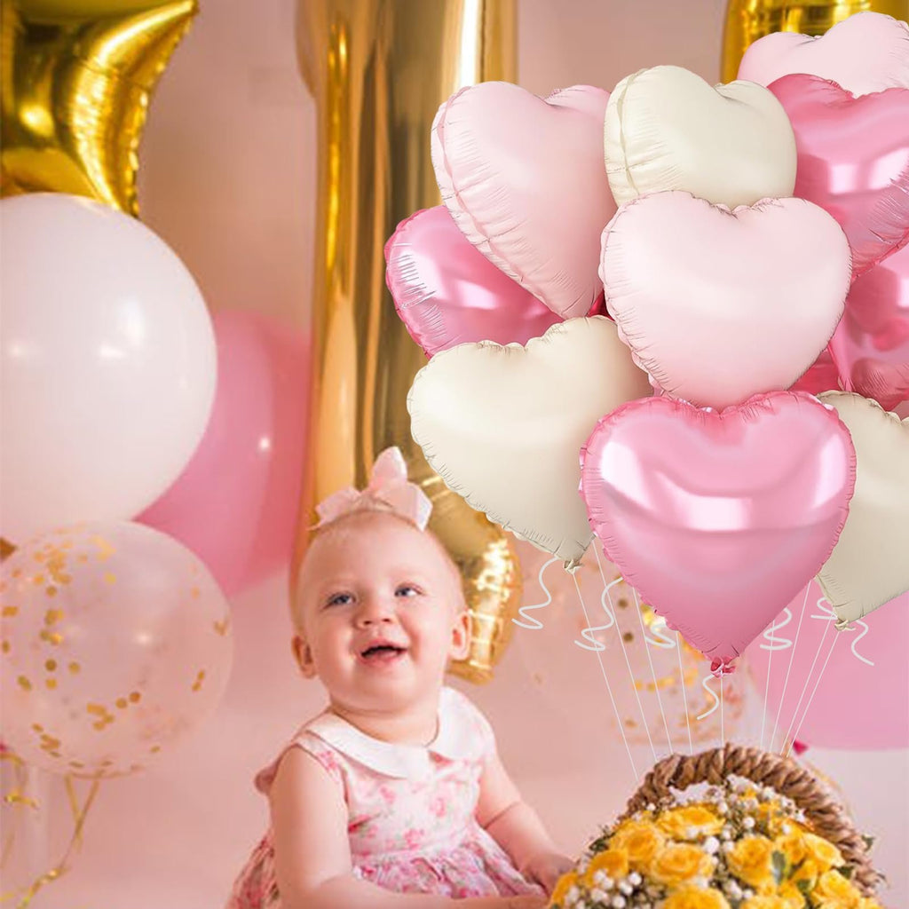 Baby girl smiling surrounded by pink and gold heart-shaped balloons and a bouquet of yellow flowers.