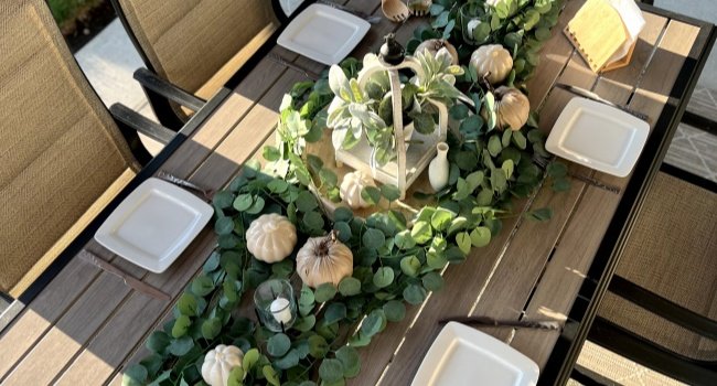 Artificial eucalyptus garland with pumpkins and a lantern arranged on an outdoor table with place settings