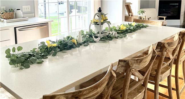Artificial eucalyptus garland with yellow flowers and white birds draped across a kitchen island with wooden chairs