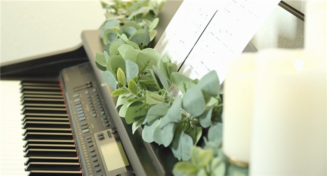 Artificial eucalyptus garland draped over a digital piano with sheet music and candles