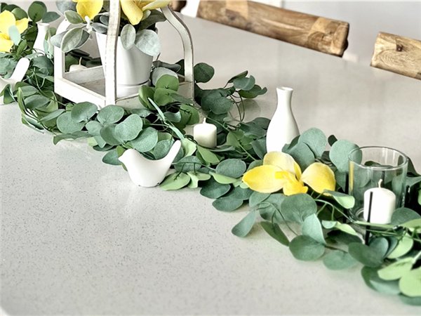 Artificial eucalyptus garland with yellow flowers and white decor on a table
