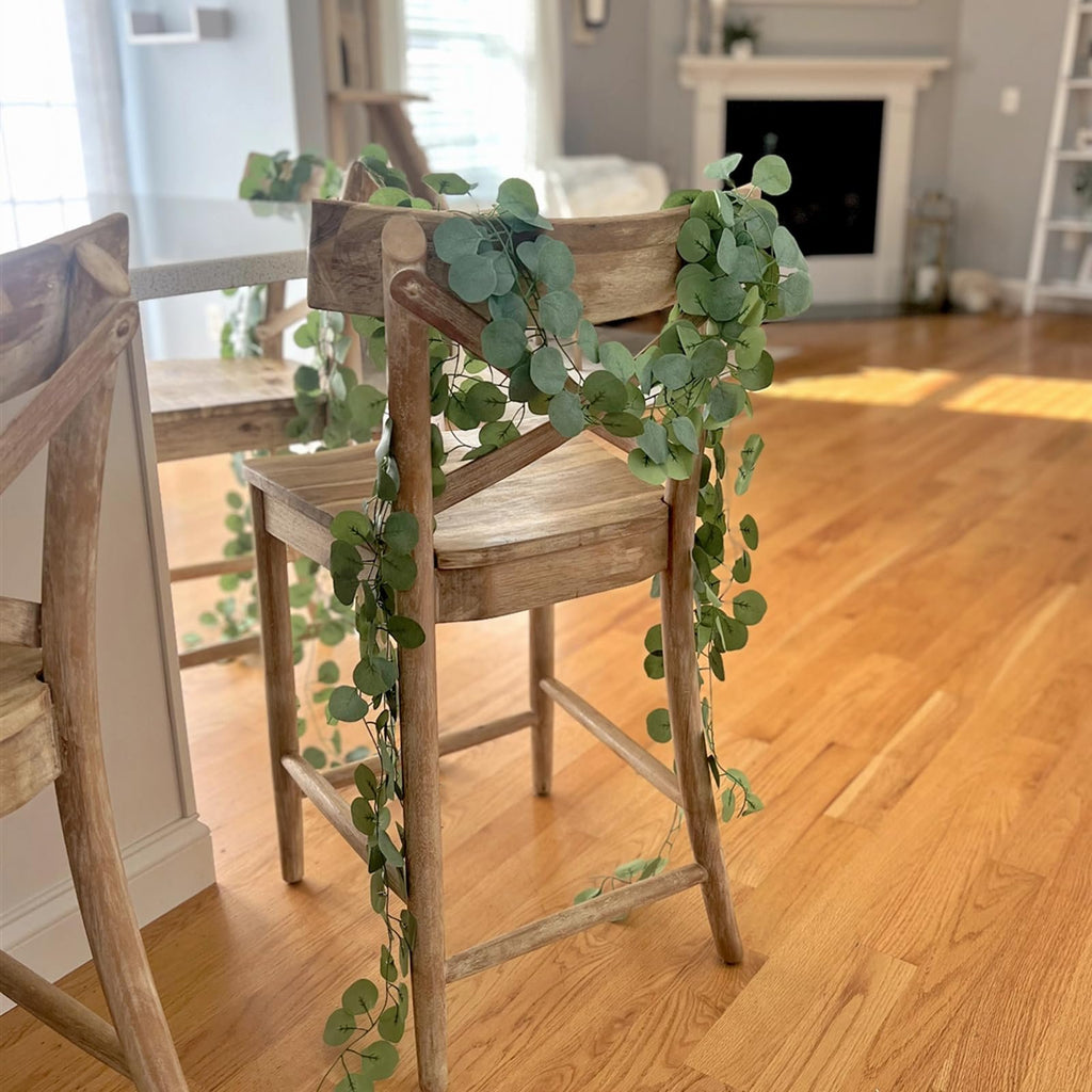 Artificial eucalyptus garland draped over a wooden chair in a sunlit room with a fireplace in the background.