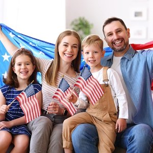 Smiling family of four holding small American flags and a large US flag indoors.