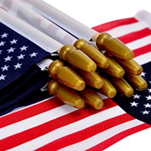 Close-up of a stack of 12 US stick flags with gold spear tops and white wooden poles, laid on top of other flags.