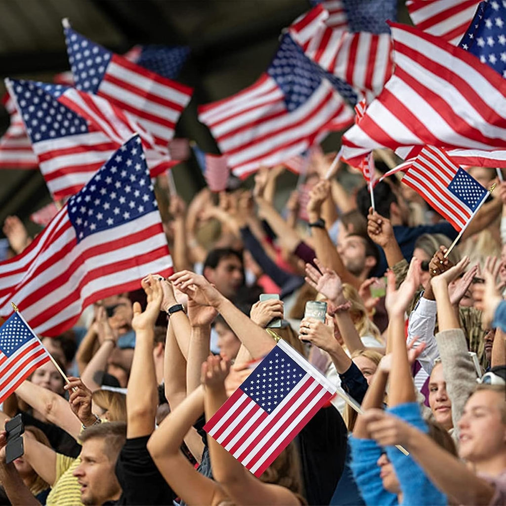 Crowd waving American flags at an event, close-up on several flags and raised hands.