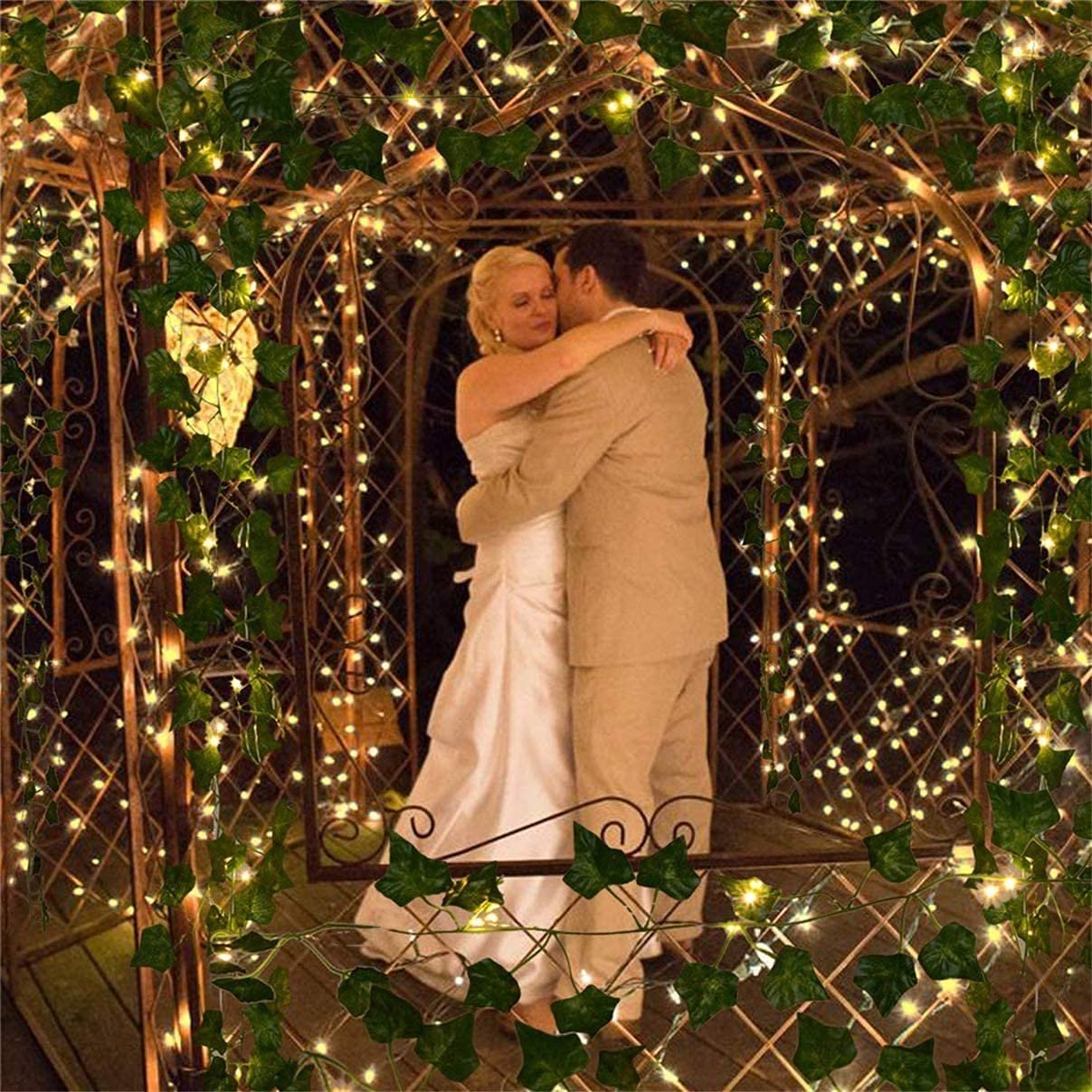 Bride and groom embracing under a gazebo decorated with artificial ivy garlands and string lights