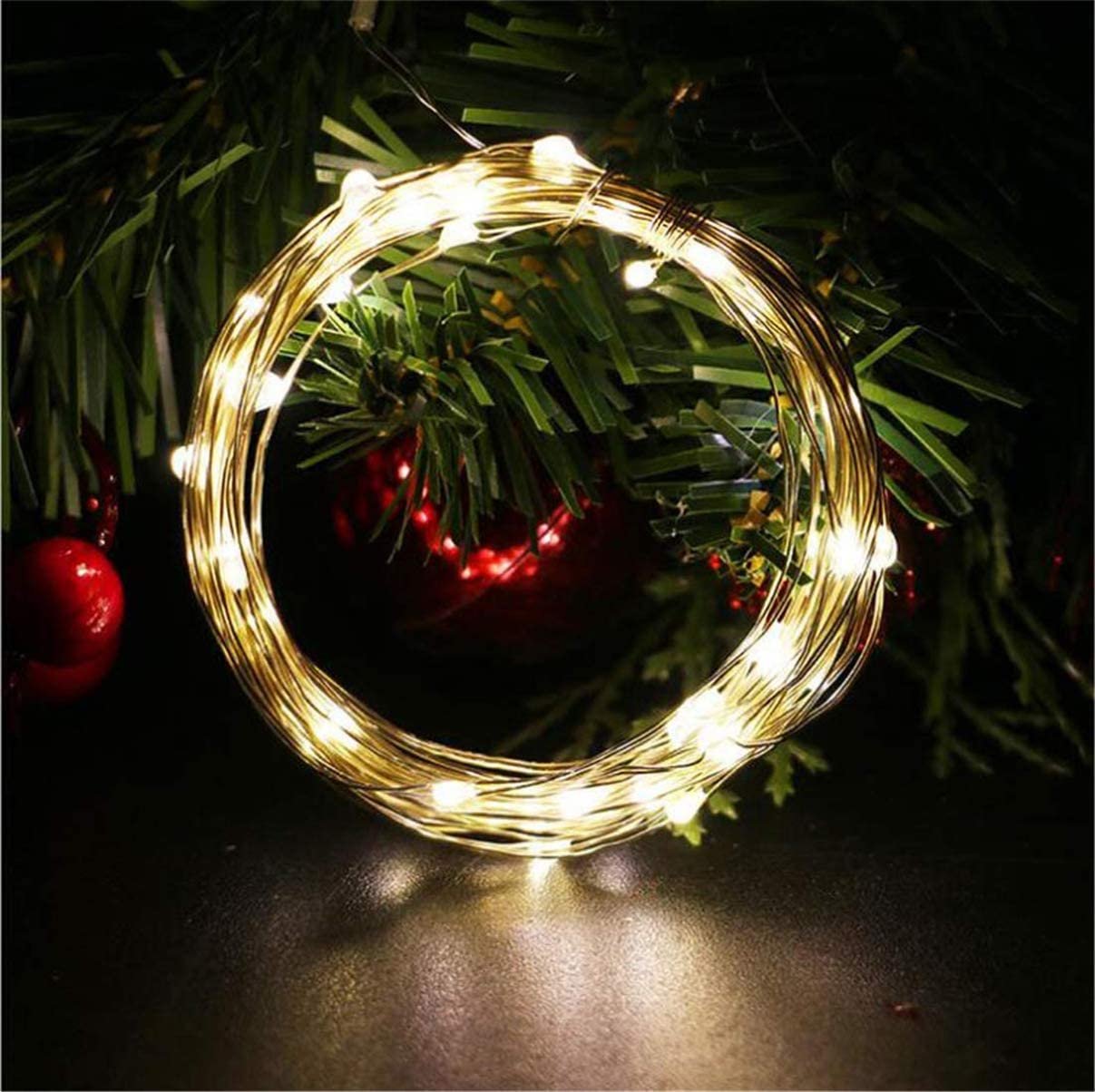 Coiled string of 100 warm white LED lights with faux greenery and red ornaments in the background