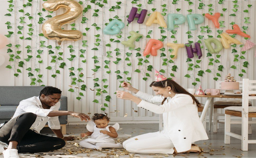 Family celebrating a birthday with artificial ivy vines and balloons decorating the wall.
