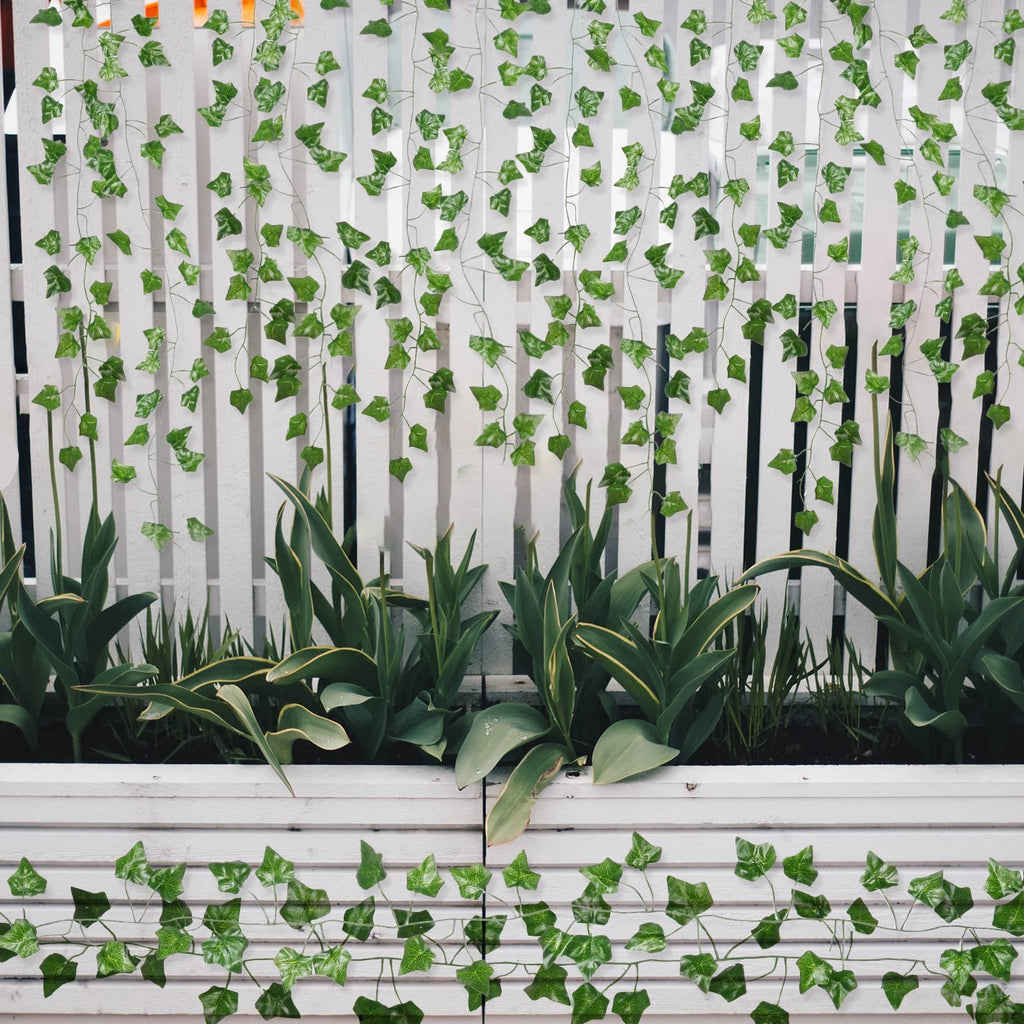 Artificial ivy vines with green silk leaves draped over a white wooden fence and planter