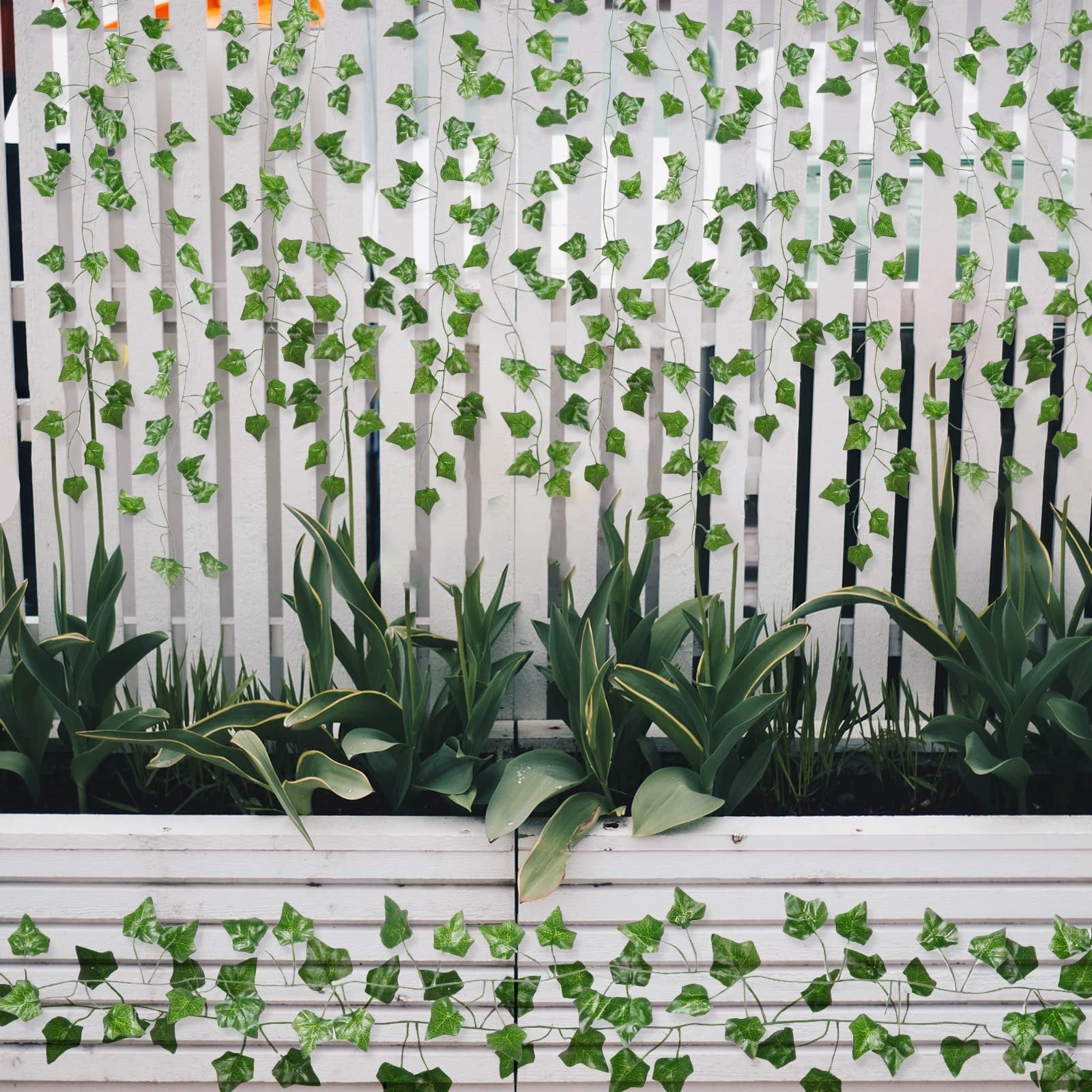 Artificial ivy vines with green silk leaves draped over a white wooden fence and planter